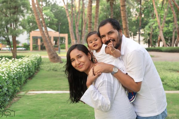 Parents cuddling their laughing toddler outdoors