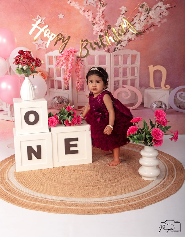 Baby seated at a pink first-birthday studio set