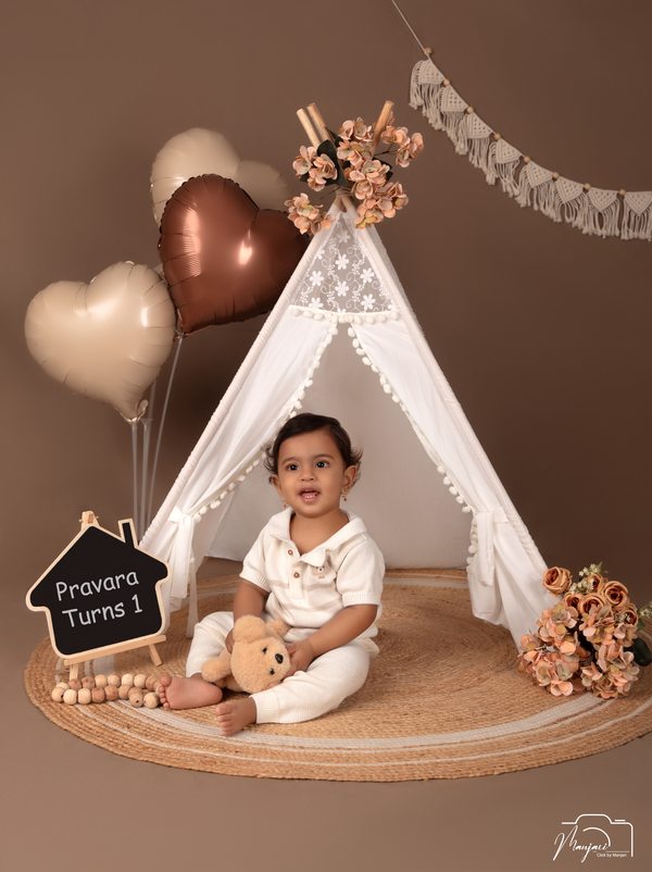 Baby seated at a neutral first-birthday teepee set