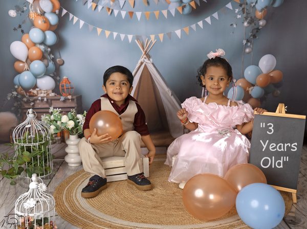 Two children together at a balloon-filled birthday set