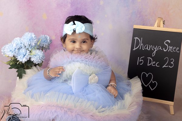 Baby in a pastel dress beside a milestone sign