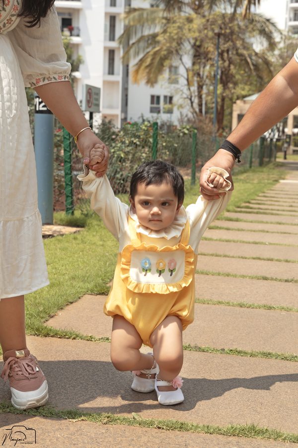 Toddler taking first steps while holding both parents hands