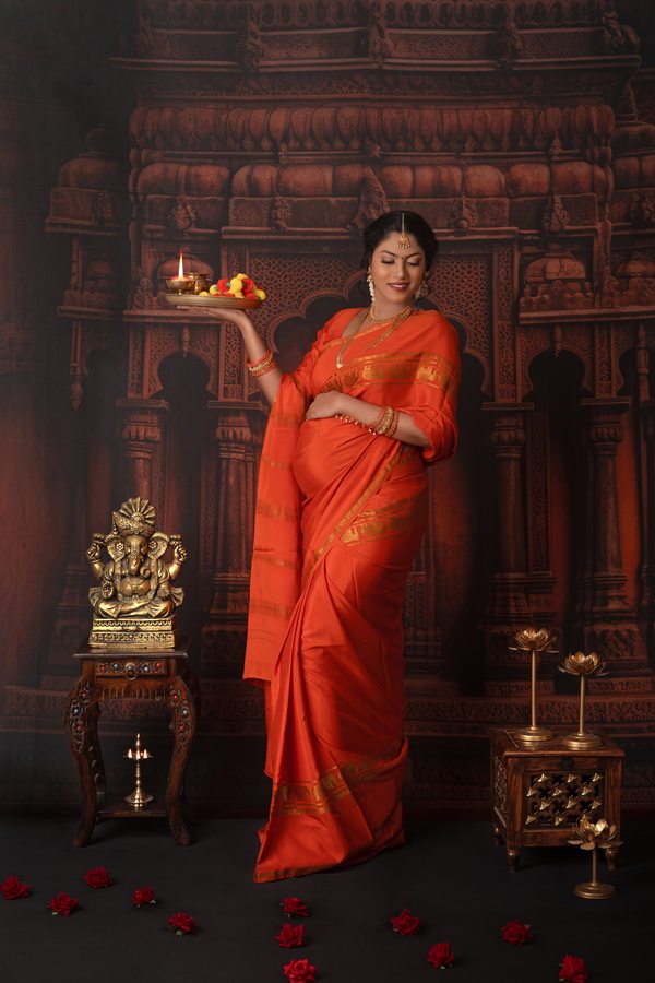 Traditional maternity portrait in a red sari with a ceremonial lamp
