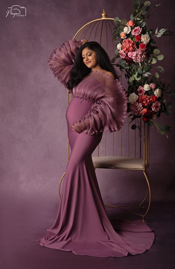 Maternity portrait in a mauve gown beside a floral peacock chair