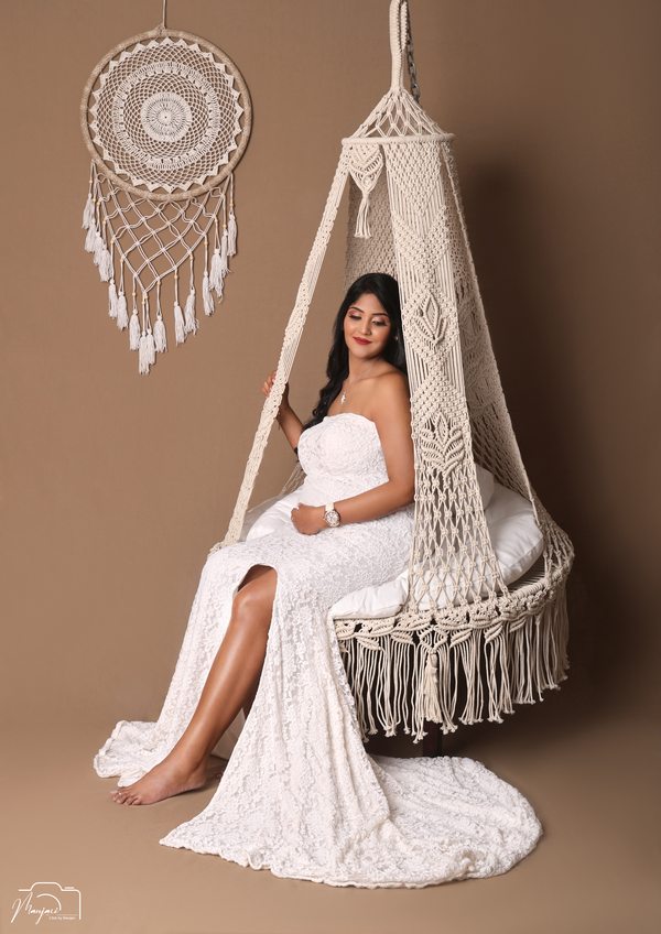 Expectant mother in a white gown seated on a macrame swing