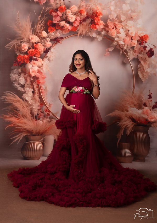 Expectant mother in a deep red gown framed by flowers