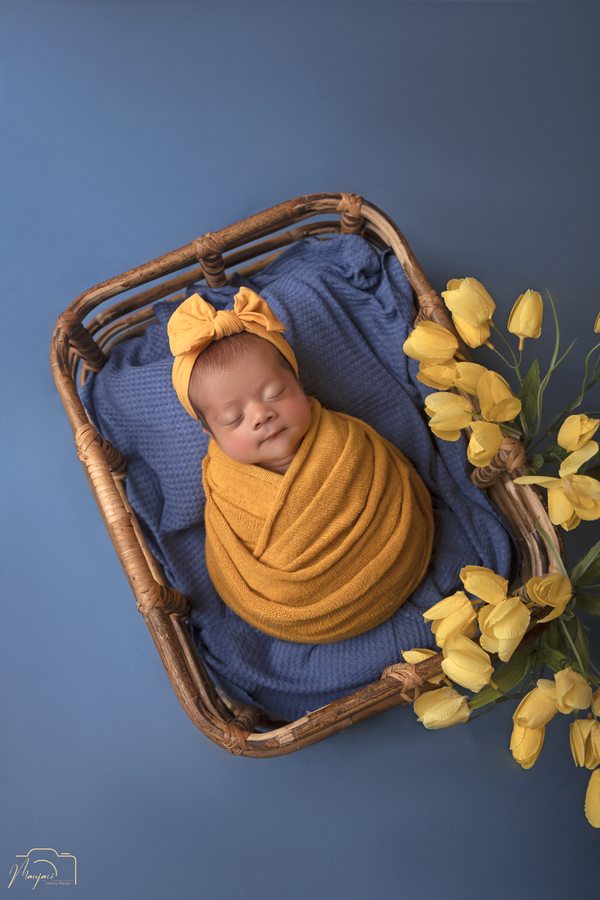 Sleeping newborn wrapped in mustard yellow in a flower-lined basket