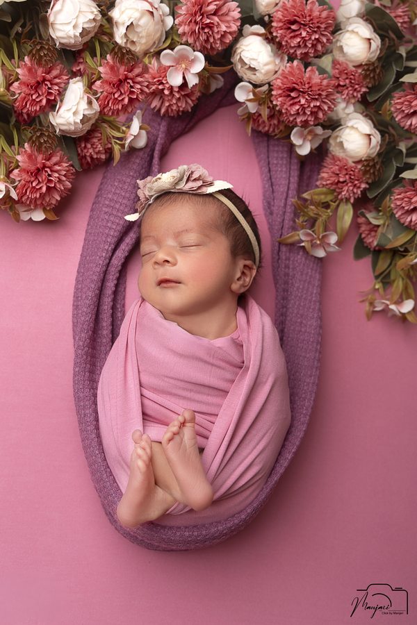Sleeping newborn wrapped in lavender beneath a floral arrangement