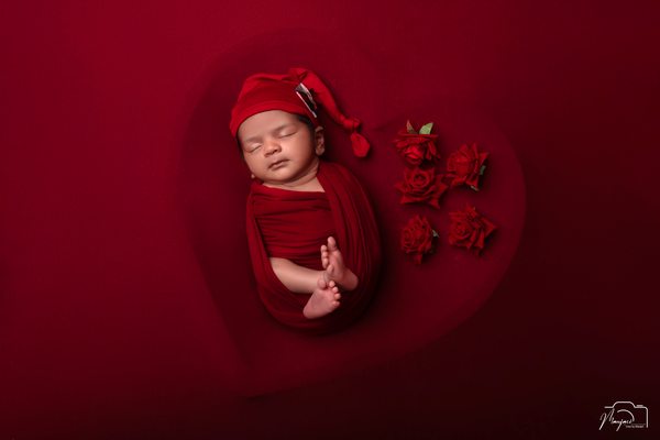 Sleeping newborn wrapped in red against a deep red background