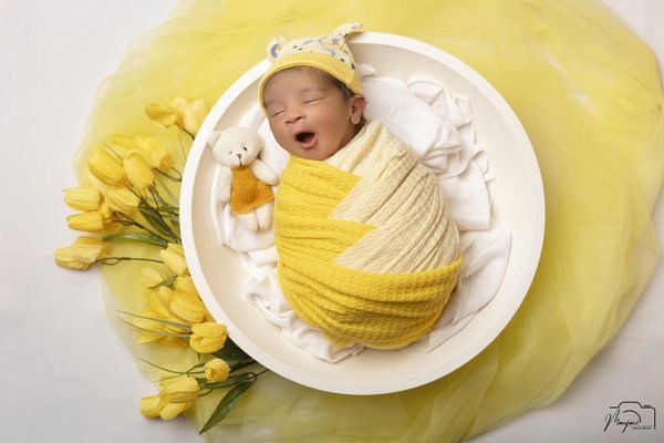 Newborn wrapped in yellow and resting in a white bowl