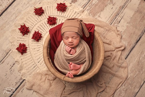 Newborn wrapped in rose fabric surrounded by red flowers