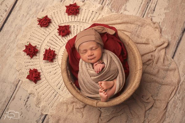 Newborn wrapped in rose fabric in a round basket