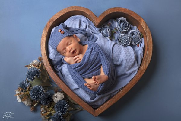 Newborn wrapped in blue in a heart-shaped basket