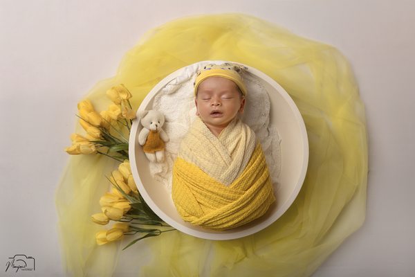 Newborn wrapped in yellow in a white bowl with flowers
