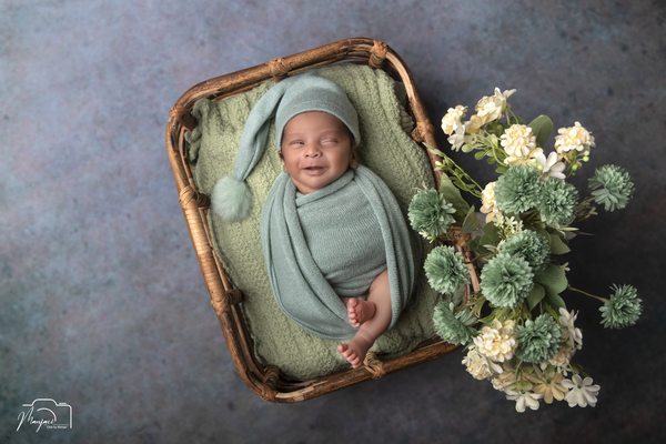 Newborn wrapped in mint green in a wicker bed with flowers