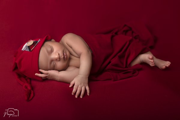 Newborn wearing a red bow against a deep red background